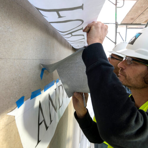 Profile shot of Adam and Javier while adjusting layout designs of all the lettering, on a wall.