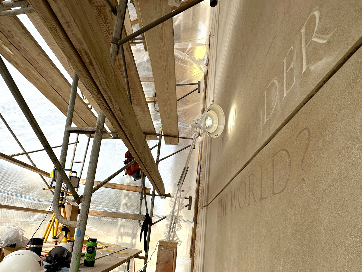 Scaffolding structure on the left side of the image, carving on a limestone wall on the right side of the picture.