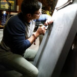 The artist carving at studio with a bright spot light pointing to the stone. He's leaning against the stone.