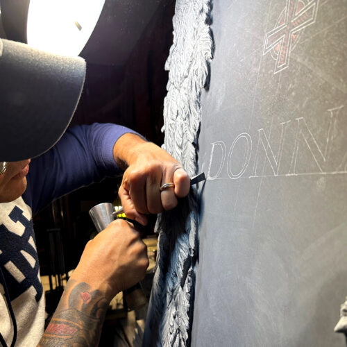 Closeup shot of Javier carving on a black slate. Silhouette of an angel sculpted.