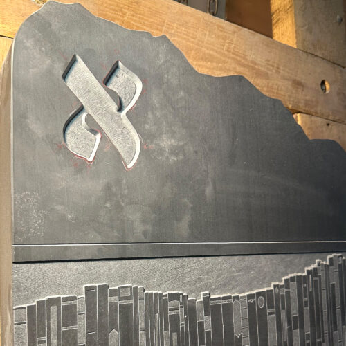Closeup detail of a Hebrew character and a bookshelf relief carving on black slate.