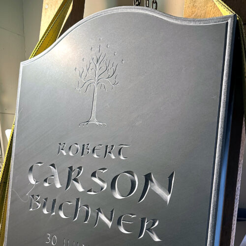 Large black slate memorial, with deep incised letters. A tree of life relief is carved above the letters.