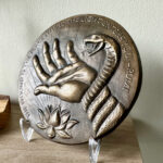 Details of a bronze medallion with a low relief hand and a snake wrapping around, raised lettering reads a Rumi poem.