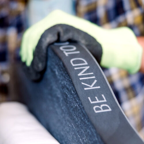 Closeup of hands holding the shoulders of a Headstone. The word Be Kind to.. is shown.