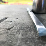 A large letter E caved into granite with a set of tools on the right hand side.