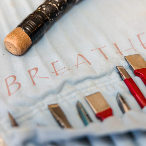 Detail shot of carving tools. The word "Breathe" is written on the blue canvas pouch.
