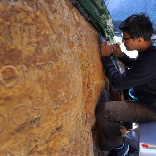 A medium shot with a depth of field, showing Javier R. Alfonzo, carving a massive granite boulder. IBIZA, SPAIN.