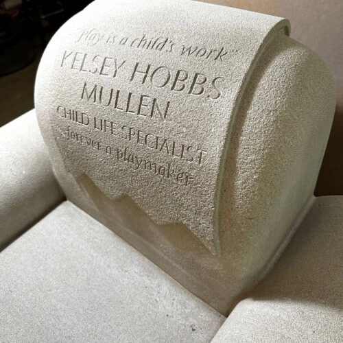 A closeup of a limestone chair with a large hand carved dedication. Installed at Hasbro Children's Hospital.