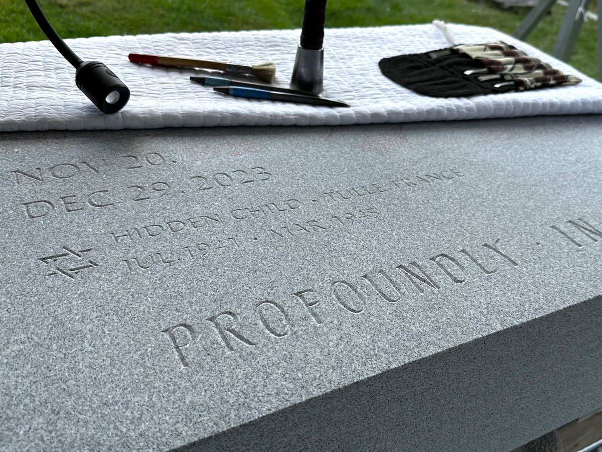 A shot of a granite stone with hand carved lettering in it. Tools of the trade in the background.