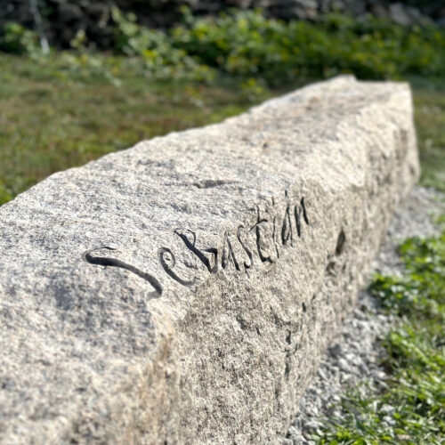 Natural granite bench memorial install in a garden. Letters carved and painted.