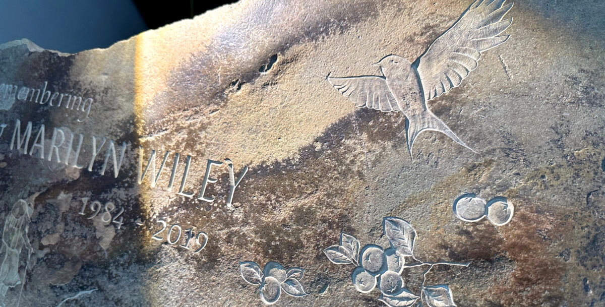 A mid shot of a sandstone memorial, various carving elements like lettering and relief are present. Stone has a natural patina color.