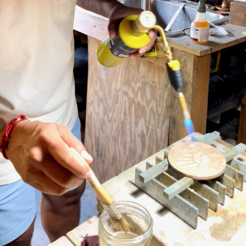 Hands shown applying a patina process to bronze medallions. A MAPP torch is adding flame.