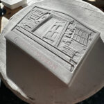 Plaster cast relief carving of a medal obverse. Details show a relief of a house porch, door and side windows.