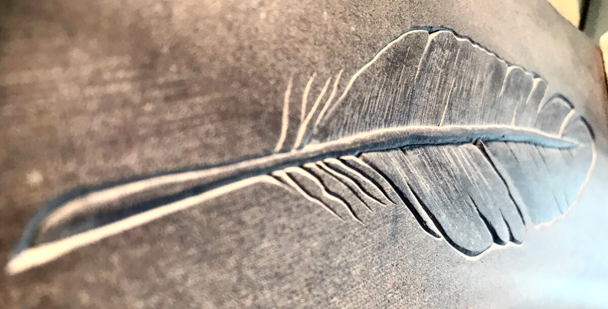 Relief carving of a feather in red slate.