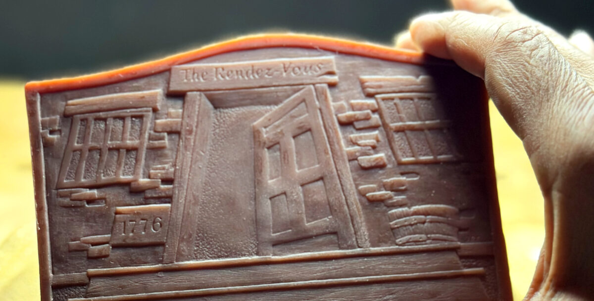 Red wax cast, detail for a bronze medallion. A hand is holding the wax.