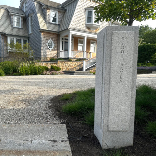 A wide shot of a granite post, the house name, carved in it and the house is blurred in the background.