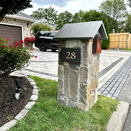 A medium shot of a mailbox post with a black slate tablet, a number 28 is carved on it and filled with light color enamel paint.