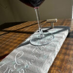 A detail closeup shot of a wine stone tablet tray with a flourished carving and a glass of wine at the end of the tray.