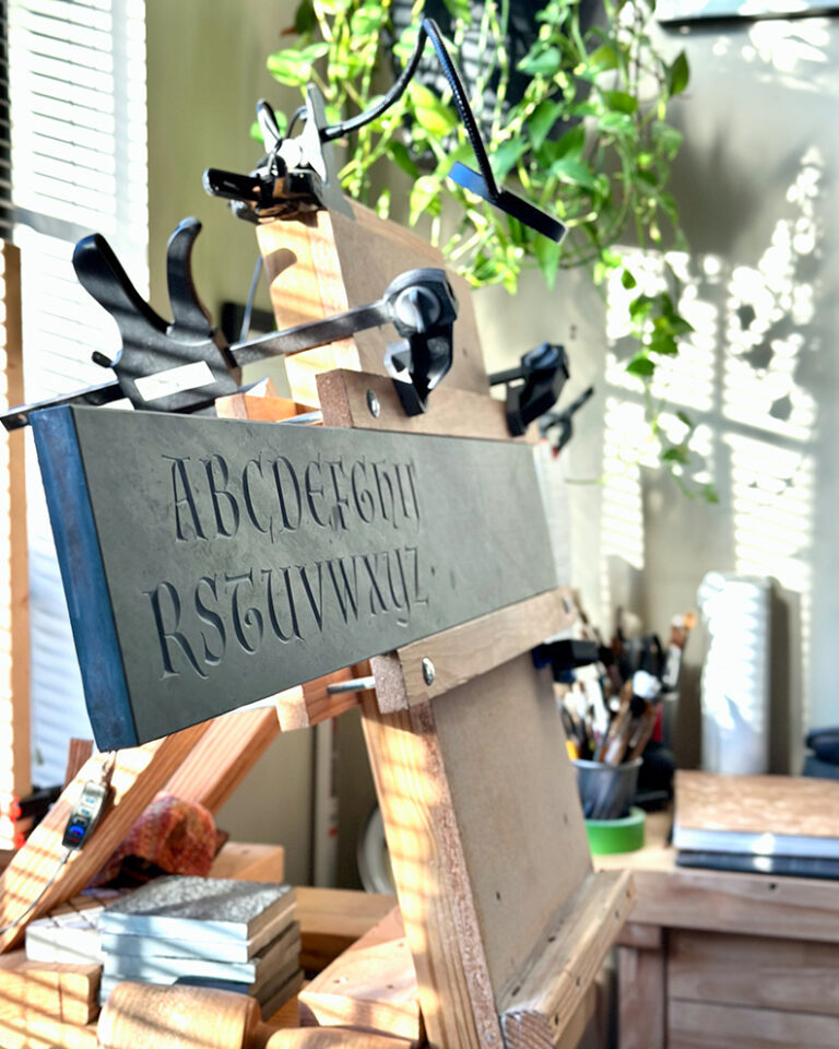 Letter carved alphabet in stone, set up on a table top wooden easel at the studio of Javier R. Alfonzo