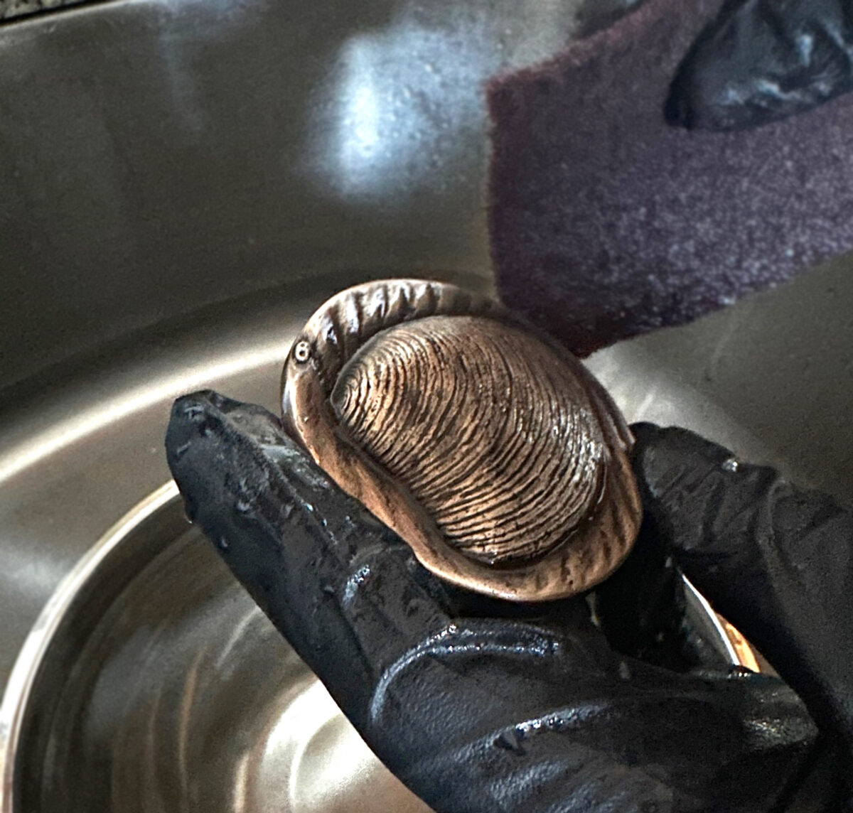Detail shot of a hand, scrubbing the patina chemicals off a bronze medallion.