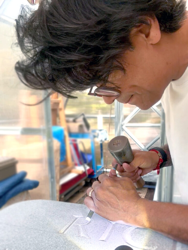 Close-up picture of the artist Javier R. Alfonzo carving on a granite memorial.