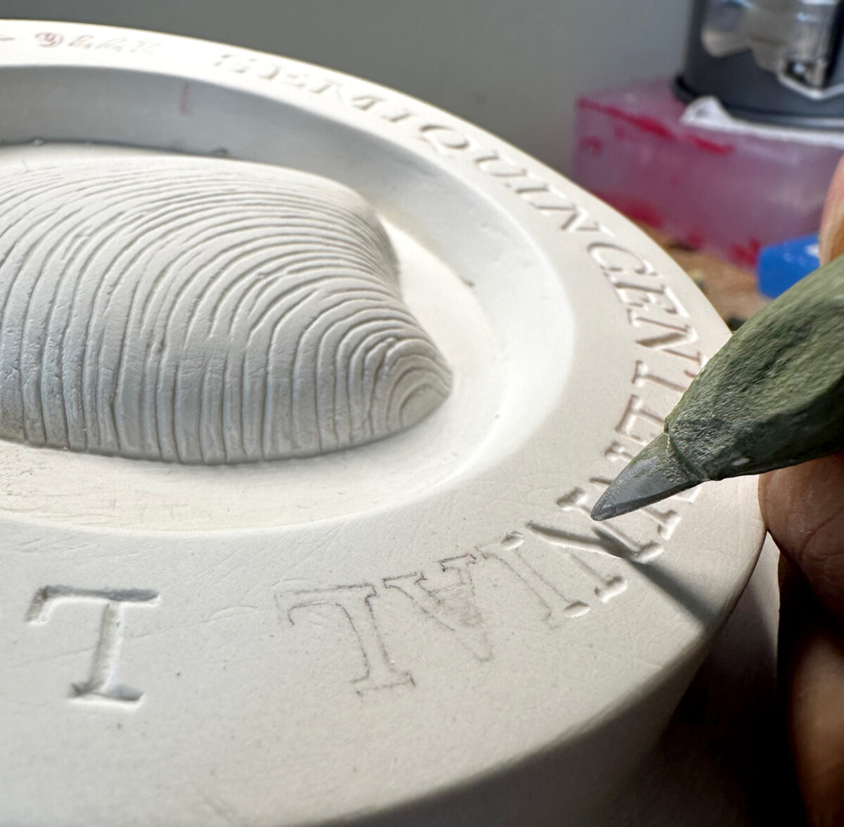 A close-up image of the process of plaster carving. Tiny letters being carved.