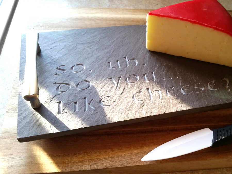 An image of a purple slate cheese tray with a waxed covered chunk of gouda cheese and the inscription "So.. do you like cheese?