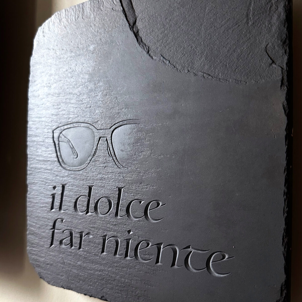 Slate stone tablet inscription with an Italian phrase "Il dolce far ninety", and a relief of sunglasses.